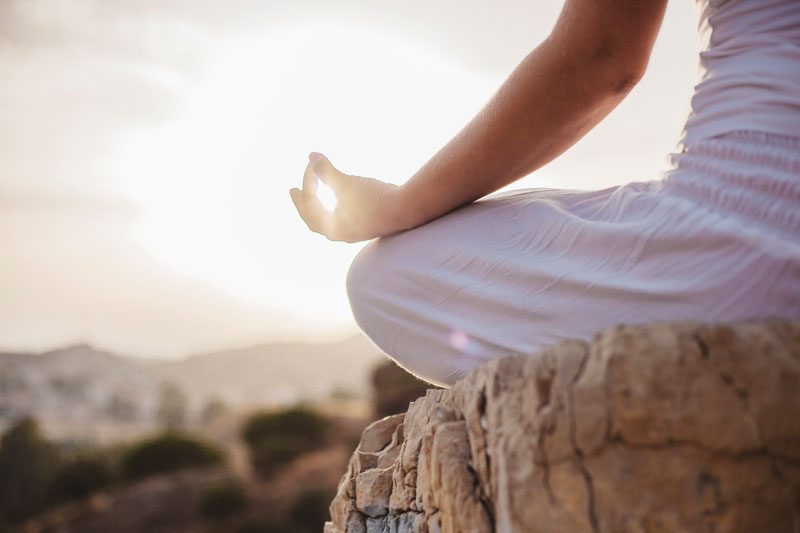Personne en méditation face au soleil couchant